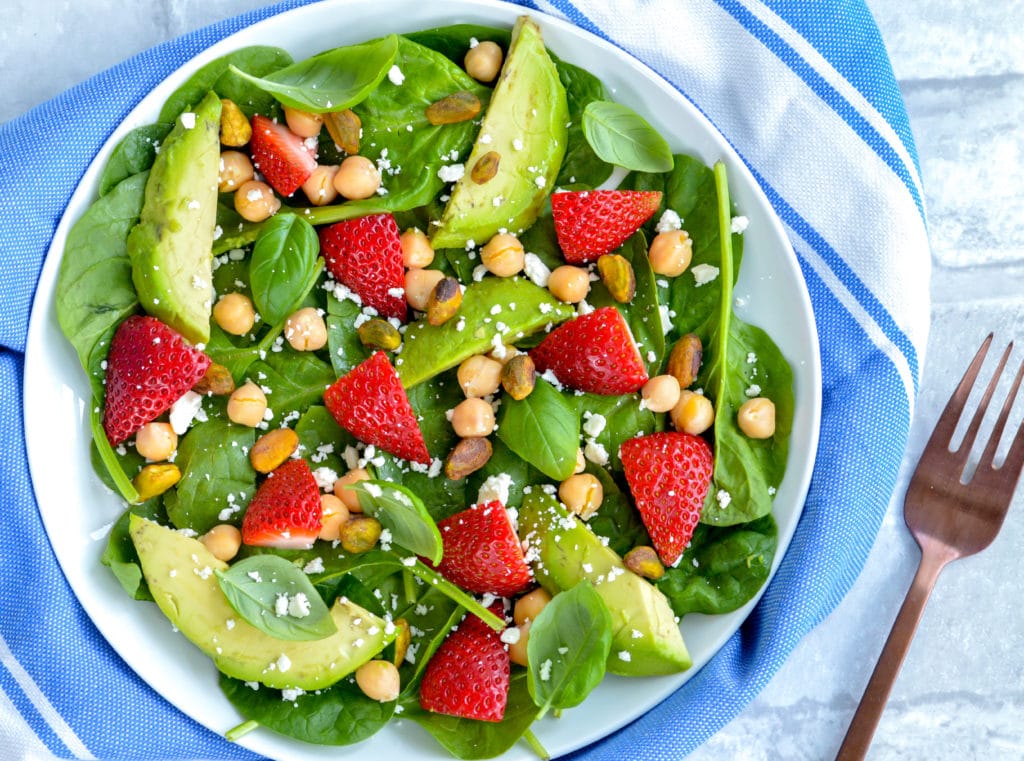 spinach salad with strawberries on a white plate 